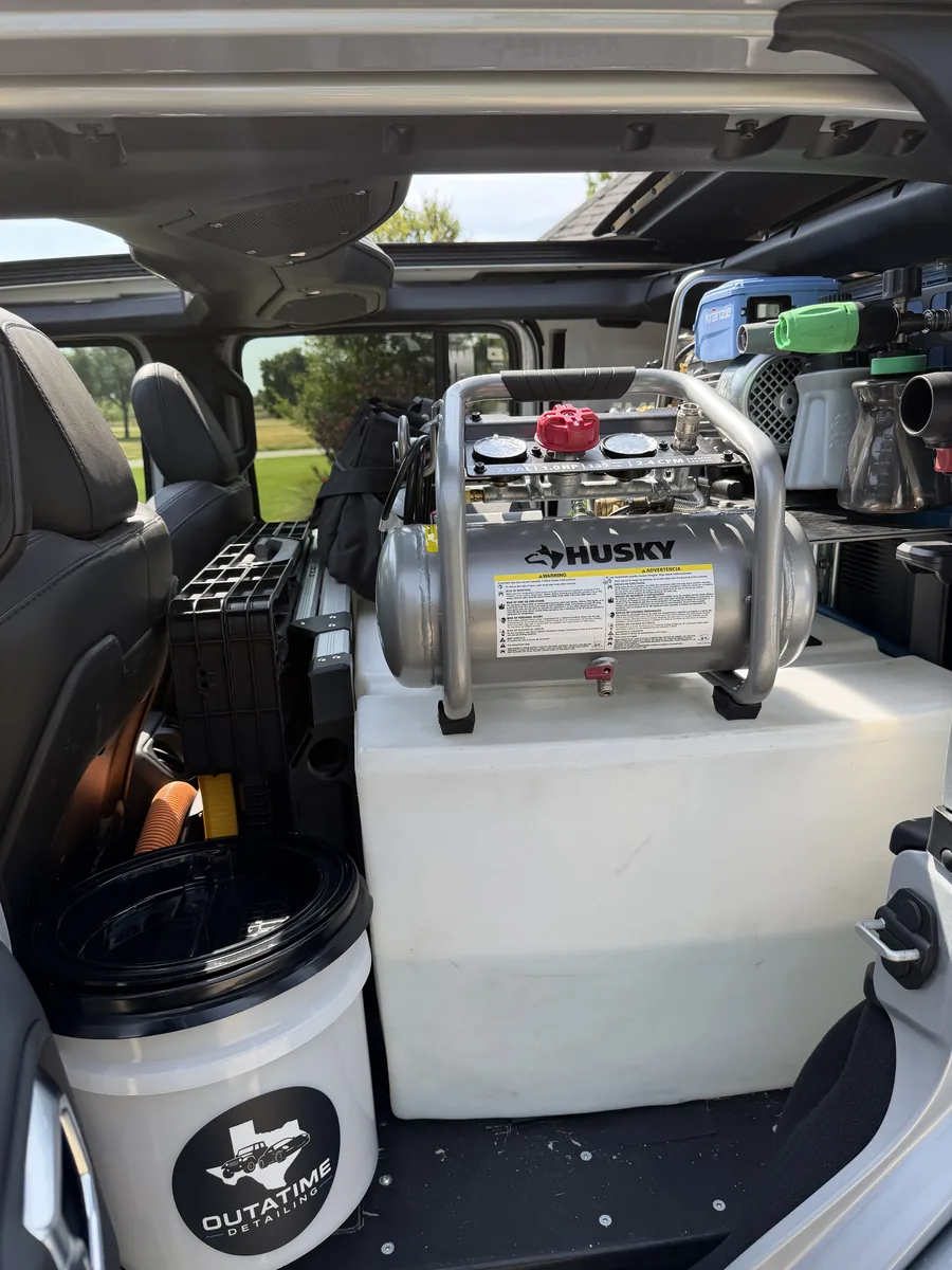 Inside the Jeep: air compressor on the water tank, next to an OutaTime Detailing bucket