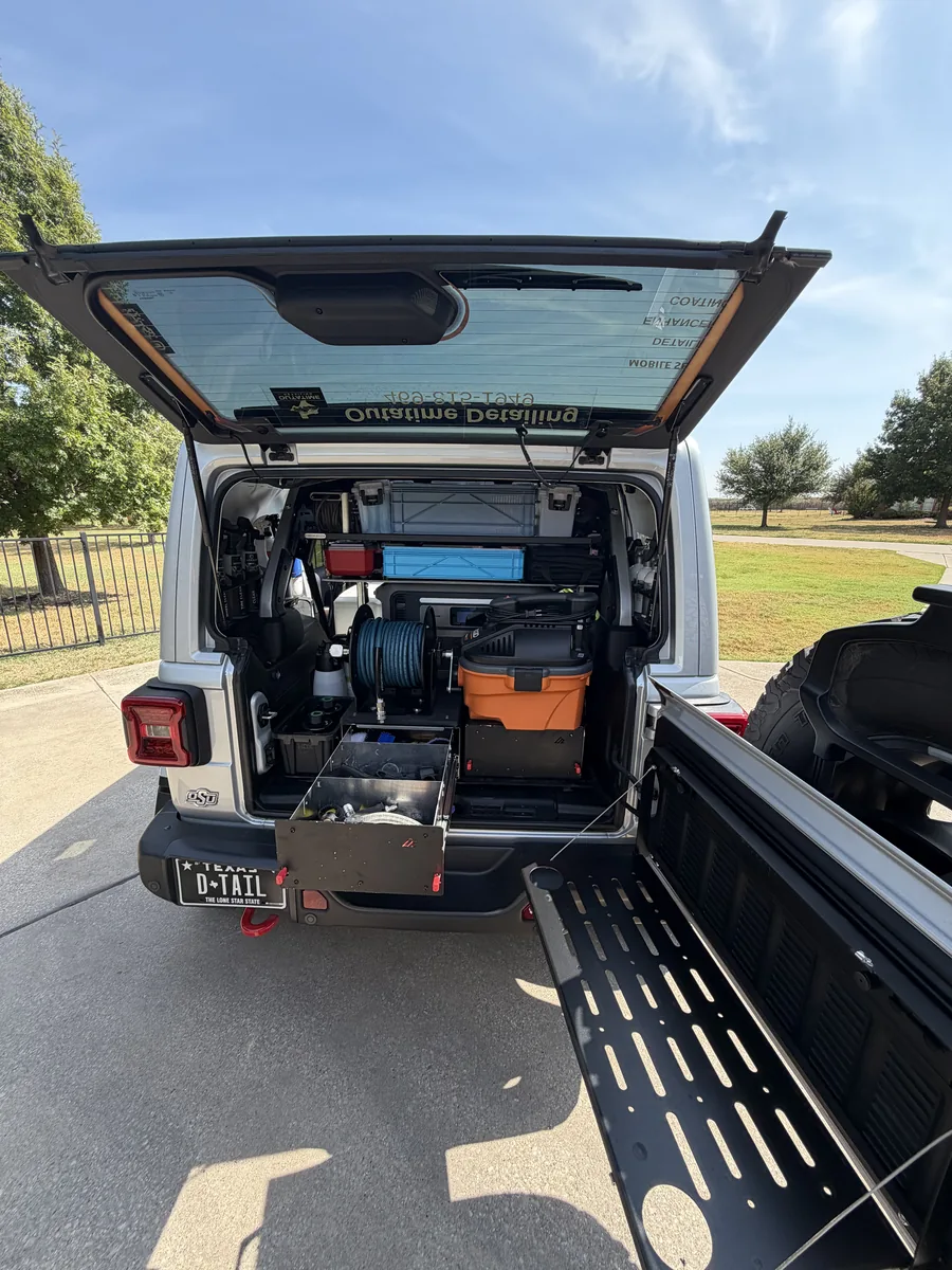 The OutaTime Jeep with the rear hatch open: storage drawers pulled out, hose reel, vacuum and a fold-down tailgate table
