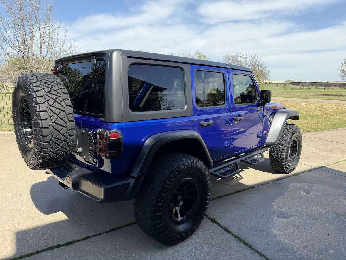 Lifted blue Jeep Wrangler, rear three-quarter view, on a residential driveway